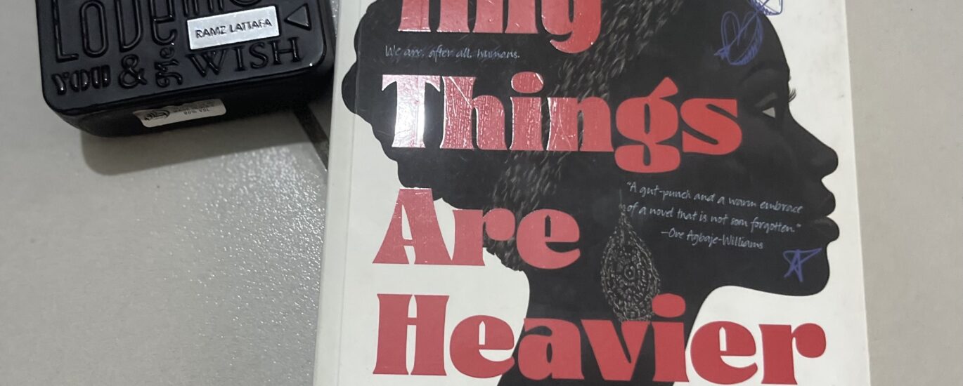 A photo of Esther Okonkwo's The Tiny Things are Heavier alongside a scent bottle on a flat grey surface.