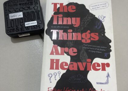 A photo of Esther Okonkwo's The Tiny Things are Heavier alongside a scent bottle on a flat grey surface.